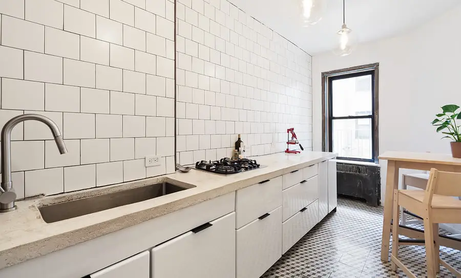 A kitchen with white cabinets and tiled walls.