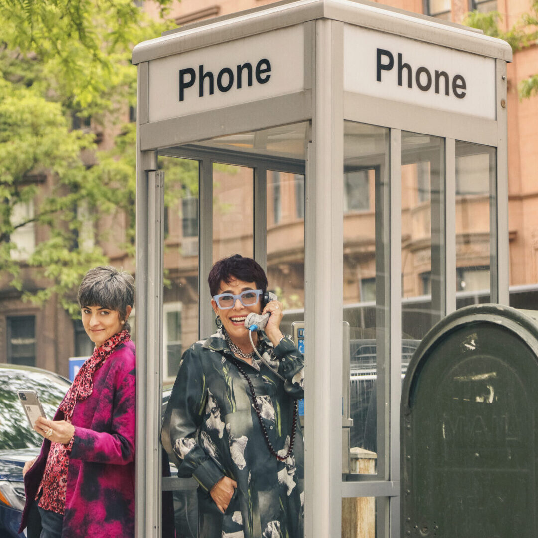 Two women are standing in a phone booth.